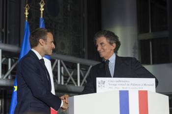 Two men, one of whom is the President of the French Republic Emmanuel Macron, shake hands on the podium